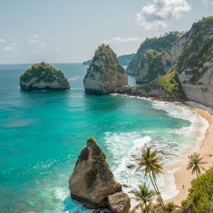 Una spiaggia sabbiosa appartata con palme, circondata da scogliere ripide e acqua turchese con grandi formazioni rocciose.