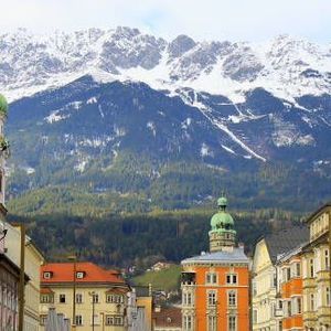 Eine Stadtstraße mit farbenfrohen Gebäuden und einem Uhrturm, vor der Kulisse großer, schneebedeckter Berge.