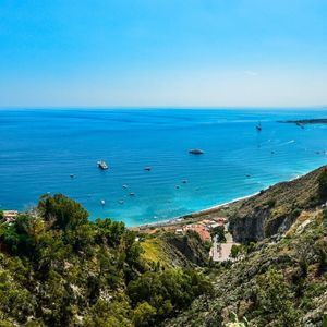 Una vista aérea de una costa donde exuberantes colinas verdes se encuentran con el mar azul brillante, salpicado de numerosas embarcaciones.