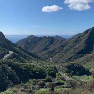 Una strada asfaltata tortuosa si snoda attraverso una catena montuosa verde e lussureggiante con l'oceano blu visibile in lontananza.