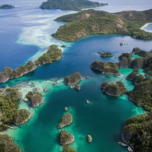 Una vista aérea de pequeñas islas rocosas cubiertas de árboles verdes, rodeadas de agua turquesa y azul profundo.