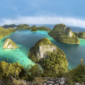 Eine Weitwinkelansicht aus erhöhter Perspektive von zahlreichen kleinen, grünen Inseln, die aus ruhigem, türkisfarbenem und blauem Meerwasser ragen.