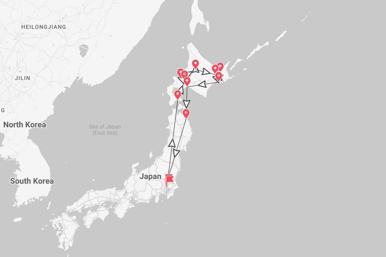 Una mappa in scala di grigi che mostra un itinerario di viaggio attraverso il Giappone, partendo dall'isola principale e girando intorno all'Hokkaido, contrassegnato da puntine e frecce rosse.