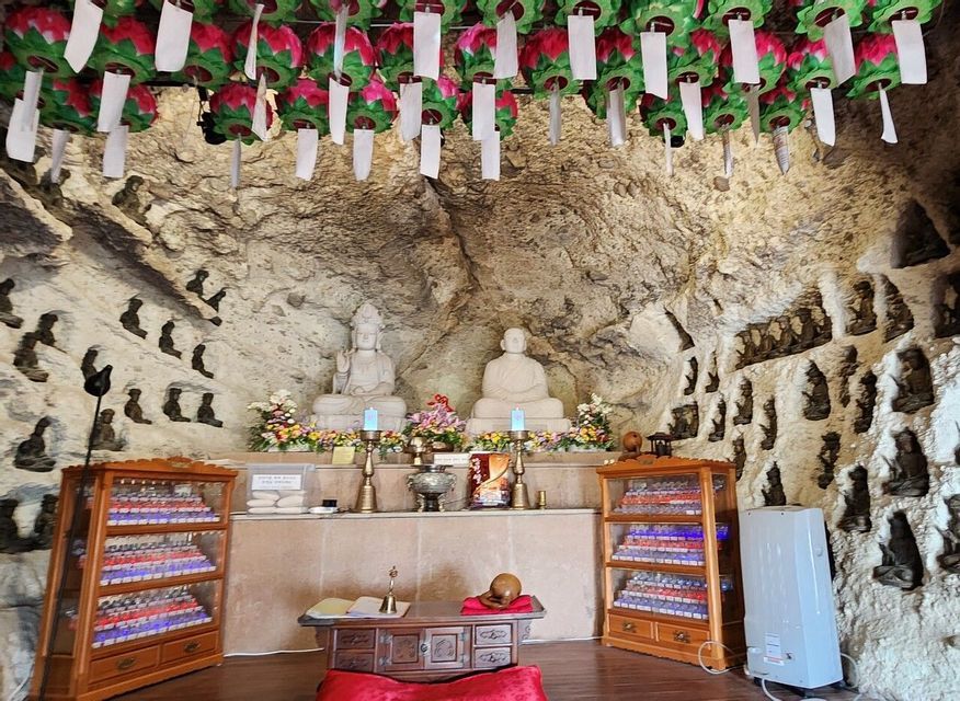 Due grandi statue di Buddha sono poste su un altare all'interno di un santuario rupestre, con piccole statue in nicchie a muro e lanterne appese al soffitto.