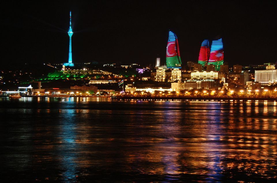 Uno skyline cittadino notturno con moderne torri ed edifici brillantemente illuminati che si riflettono nell'acqua.
