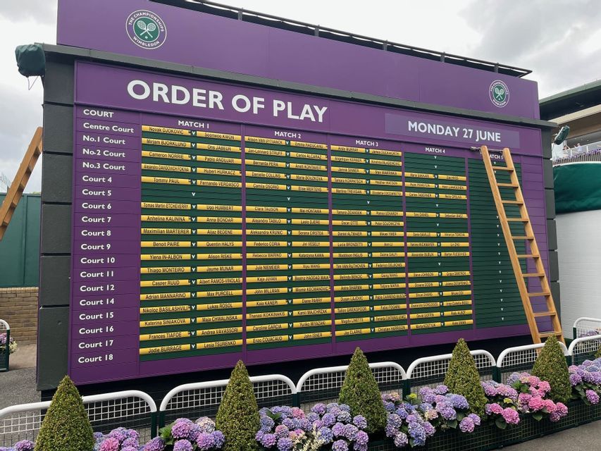 Il tabellone tradizionale viola e verde 'Order of Play' del torneo di tennis di Wimbledon, con ortensie in primo piano.
