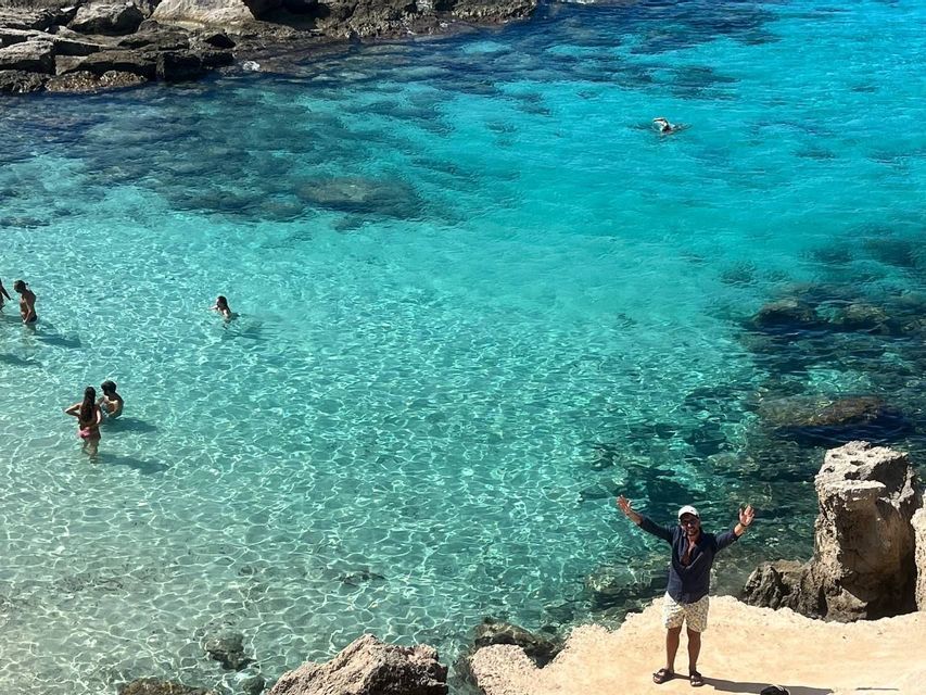 Un hombre posa en un acantilado rocoso mientras un grupo de WeRoad nada en el mar turquesa cristalino.