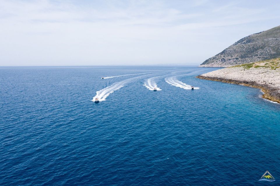 Vista aerea di cinque motoscafi di un viaggio di gruppo WeRoad che navigano sul mare blu, lasciando scie bianche vicino a una costa rocciosa.