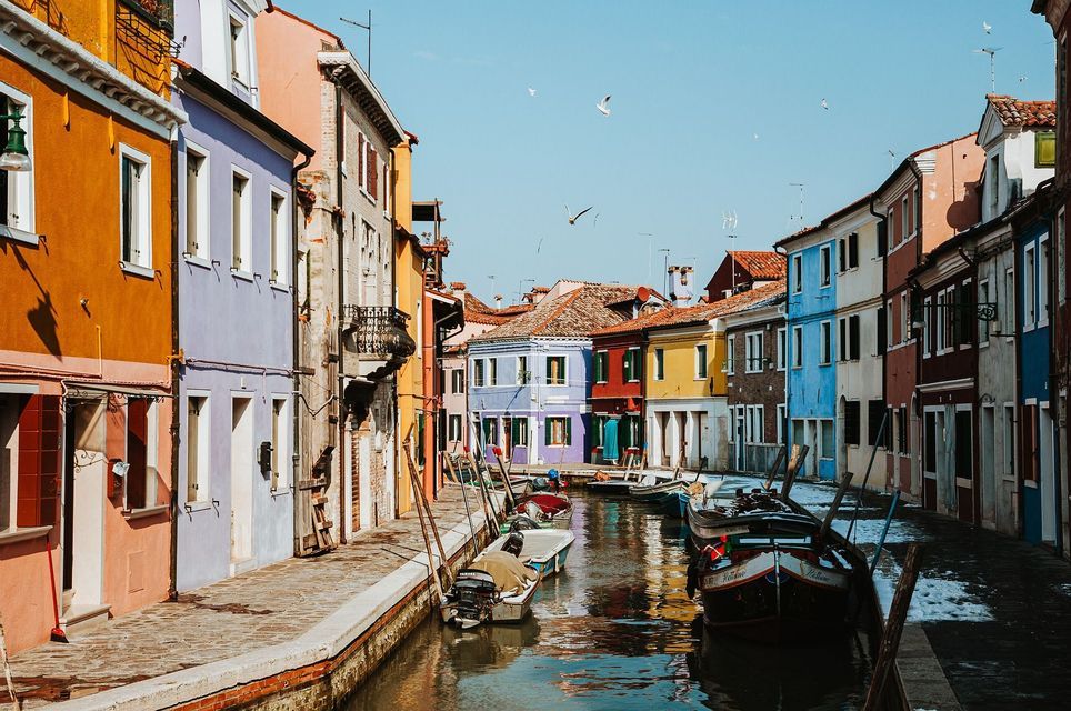 Barche ormeggiate in uno stretto canale fiancheggiato da edifici vivaci e multicolori sotto un cielo limpido.