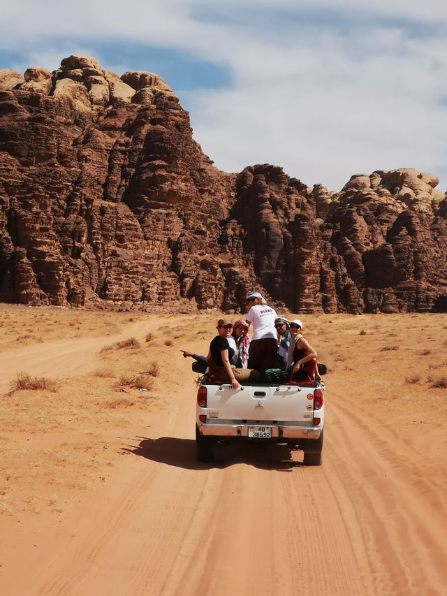 Un voyage de groupe WeRoad à l'arrière d'un pick-up blanc sur une route sablonneuse à travers un désert rocheux.