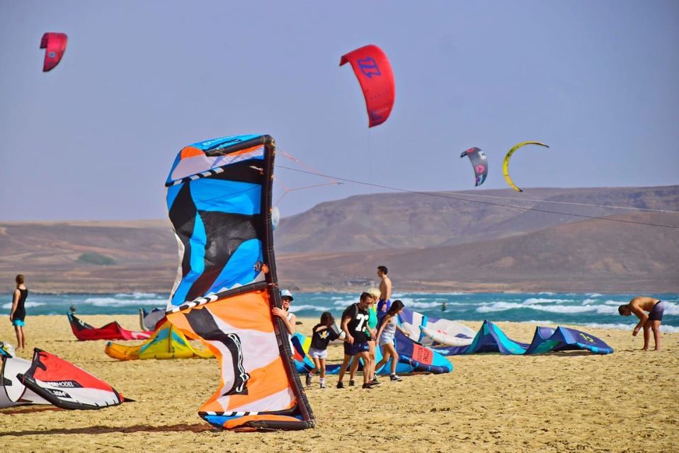 Un viaggio di gruppo WeRoad si prepara per il kitesurf su una spiaggia sabbiosa, con aquiloni colorati sulla sabbia e in aria.