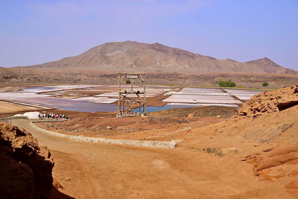 Un viaggio di gruppo WeRoad si affaccia su vaste saline e un'antica torre di legno, in una valle arida con una catena montuosa alle spalle.