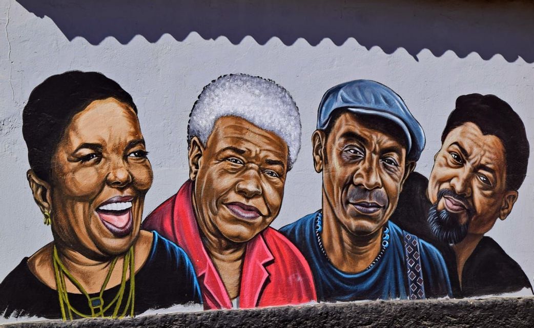 Un murale colorato su una parete bianca, che raffigura dettagliati ritratti di quattro persone nere sorridenti.