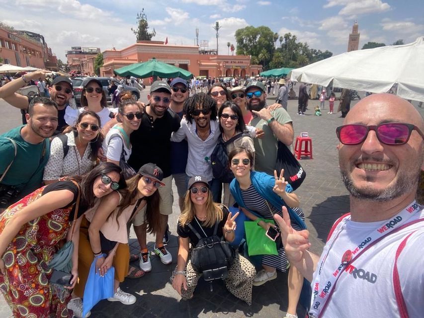Eine große WeRoad-Gruppenreise lächelt und posiert für ein Selfie auf einem belebten Stadtplatz an einem sonnigen Tag.