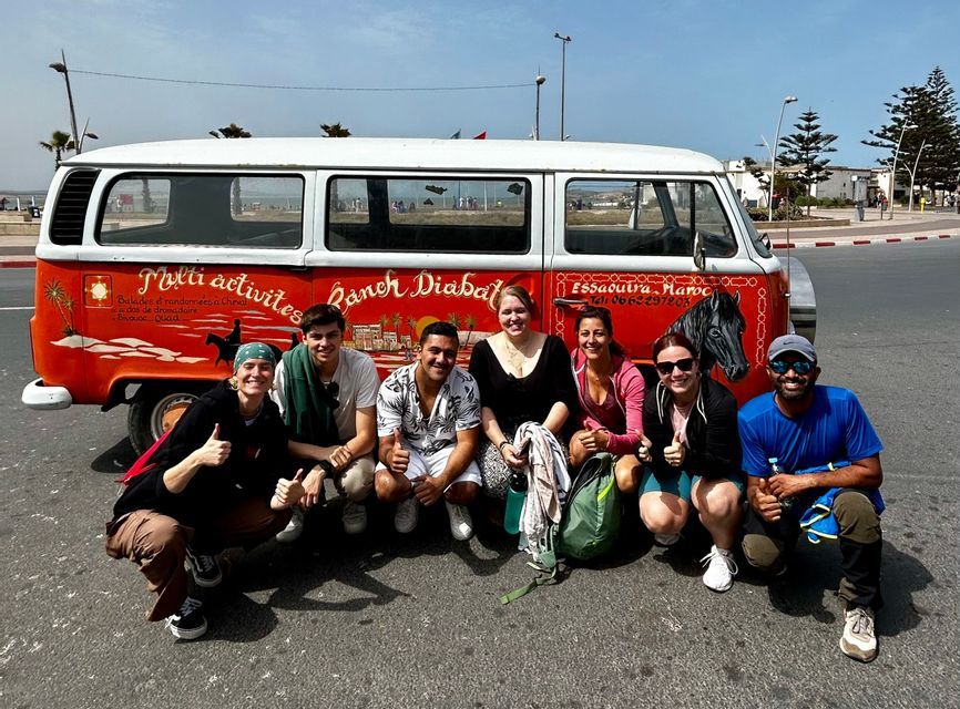 A WeRoad group trip smiling and crouching for a photo in front of a vintage red and white van on a paved street.