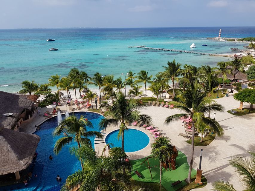 Una vista aerea di un resort tropicale sulla spiaggia con piscine, palme e una spiaggia di sabbia bianca accanto a un oceano turchese.