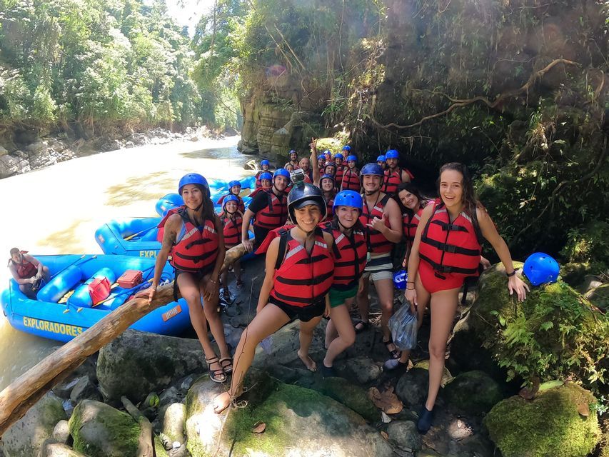 Un groupe WeRoad en pleine aventure, équipé de gilets de sauvetage rouges et de casques bleus, prend la pose pour une photo sur la rive rocheuse d'une rivière, à côté de leurs bateaux gonflables.