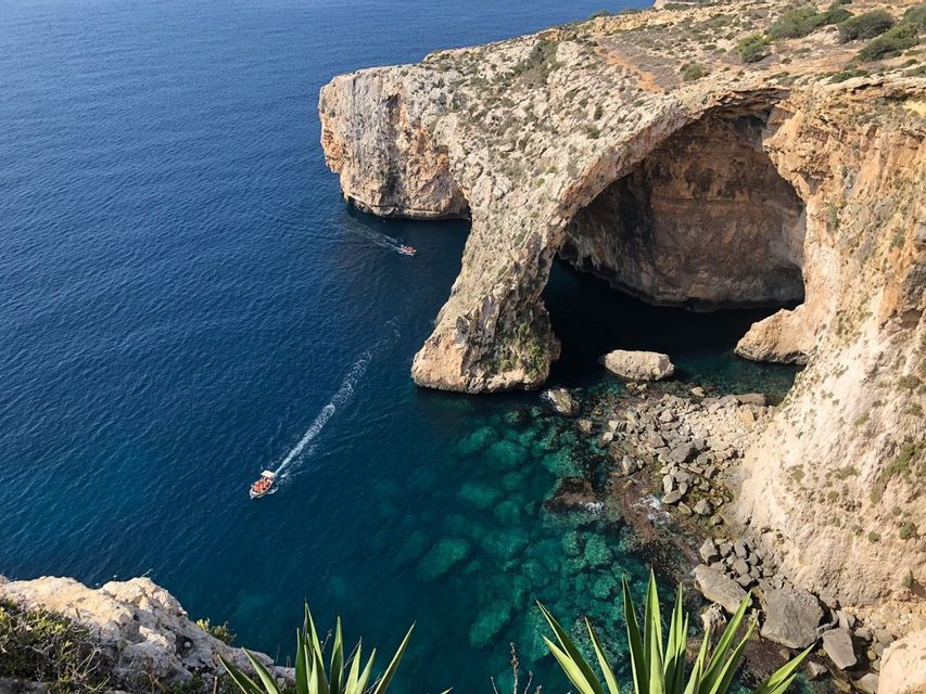 Eine Luftaufnahme eines großen natürlichen Felsbogens über dem Meer, mit zwei Booten, die durch das klare türkisfarbene Wasser fahren.