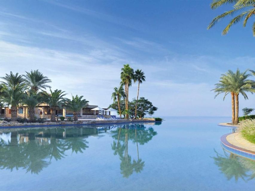 Una piscina a sfioro in un resort sul mare, con palme e i loro riflessi sull'acqua calma.
