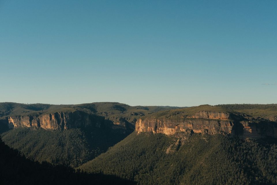 The escarpment above the valley A long sandstone escarpment dropping into a forested valley in the Blue Mountains, seen from the rim.