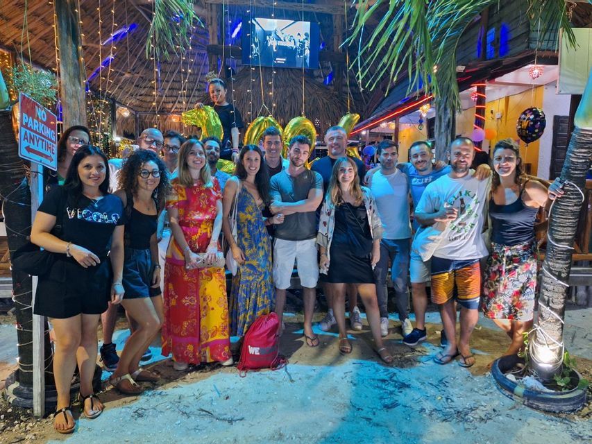 Un gruppo WeRoad in posa per una foto su una spiaggia sabbiosa di notte, festeggiando con grandi palloncini dorati del '30'.