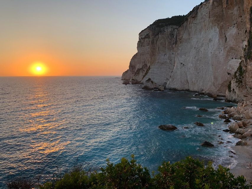 Il sole tramonta su un oceano calmo accanto a imponenti scogliere bianche di calcare sotto un cielo limpido.