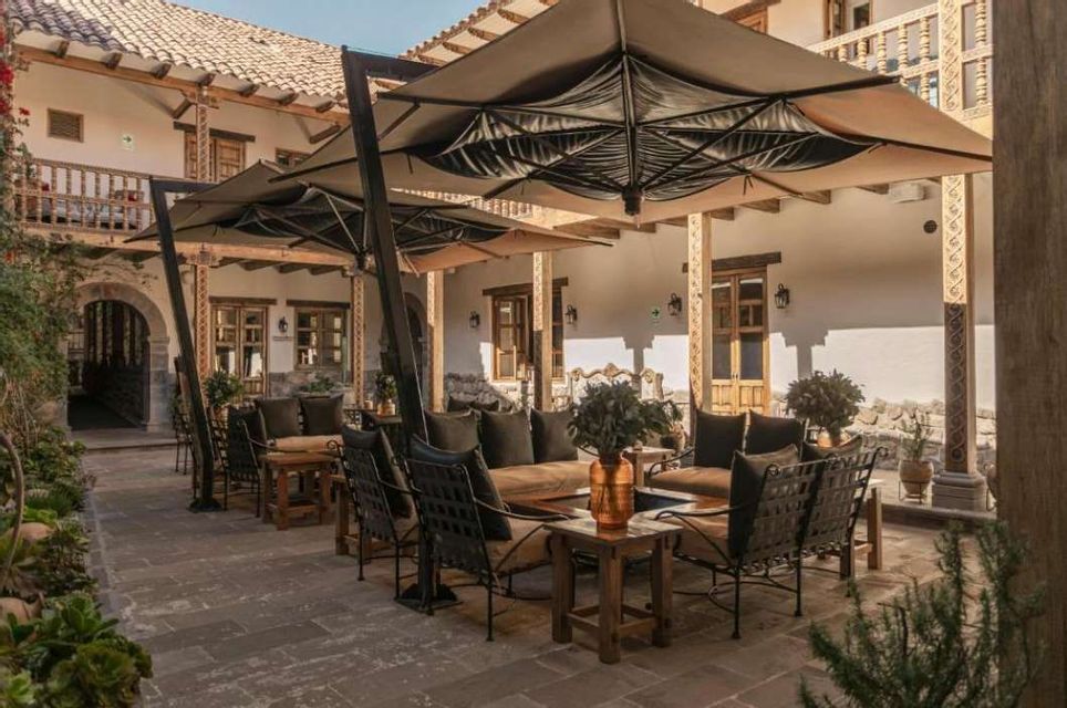 Un patio esterno con sedie a sdraio, divani e grandi ombrelloni allestito nel cortile di un edificio tradizionale.
