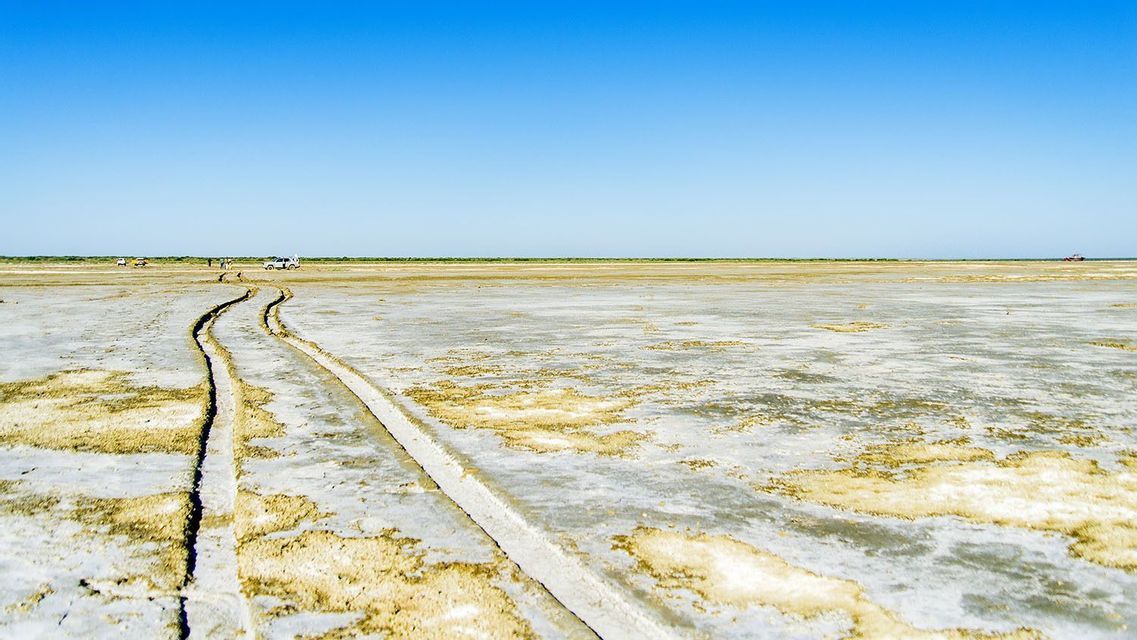 Tire tracks run through a vast salt flat towards a WeRoad group trip and their off-road vehicles under a clear blue sky.