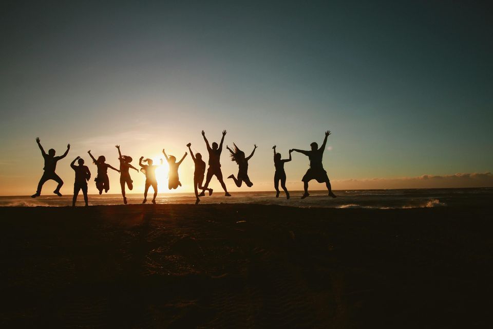 Un viaggio di gruppo WeRoad con persone in silhouette che saltano su una spiaggia al tramonto.