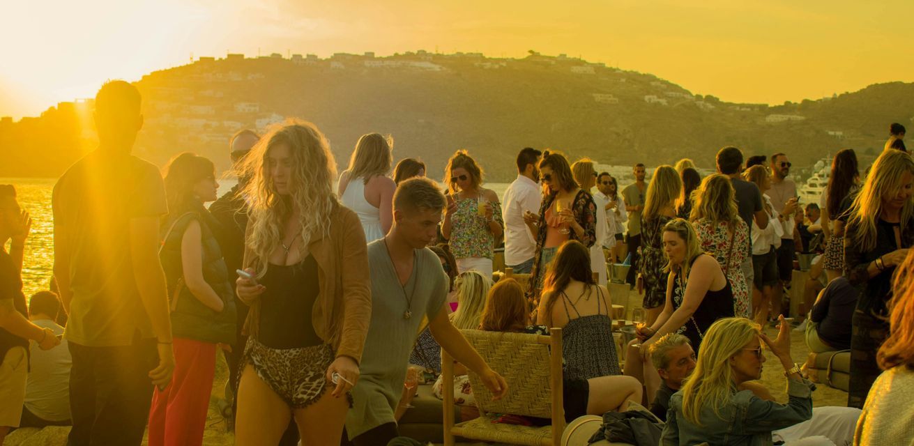 Un viaggio di gruppo WeRoad che socializza a una festa in spiaggia durante un tramonto dorato, con colline sullo sfondo.