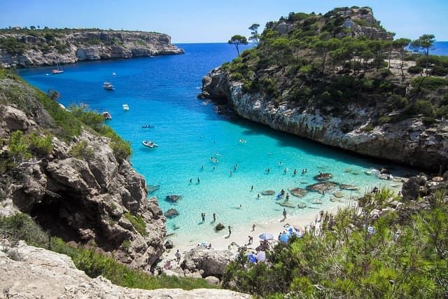 Vista elevada de una cala recóndita con aguas turquesas y cristalinas, donde la gente nada y se relaja en una pequeña playa de arena.