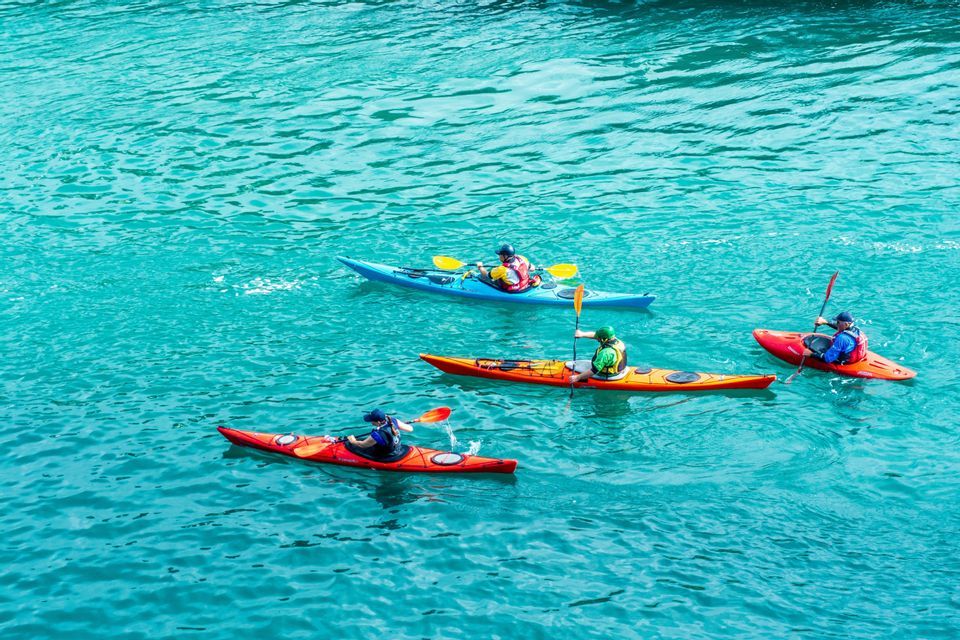 Desde arriba, cuatro personas en un viaje grupal de WeRoad reman kayaks de colores en aguas turquesas.
