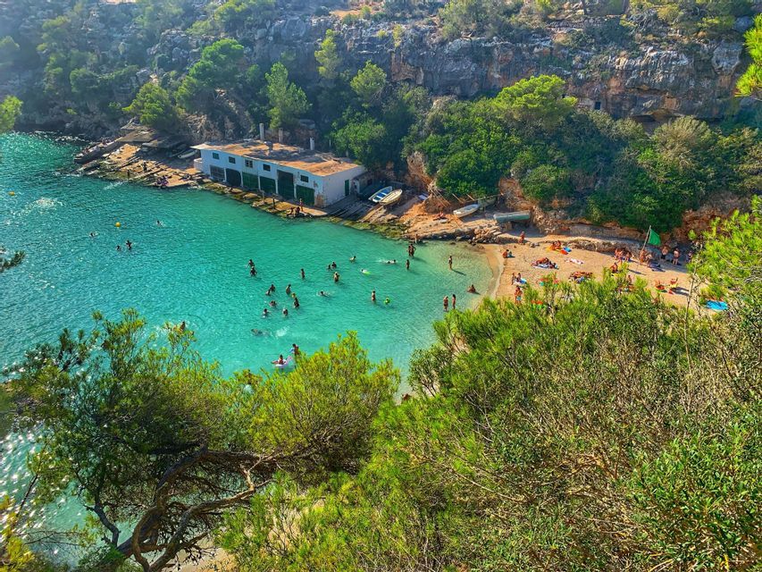 Una vista elevada de una cala apartada donde la gente nada en aguas claras de color turquesa y se relaja en una pequeña playa de arena.