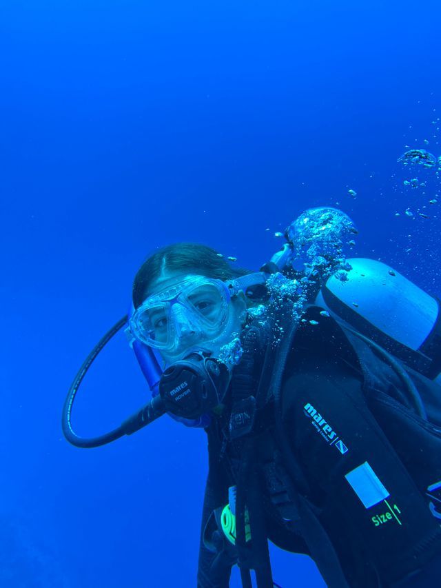 Una toma de primer plano de un buzo con máscara y regulador, flotando bajo el agua en aguas azul profundo con burbujas ascendiendo.