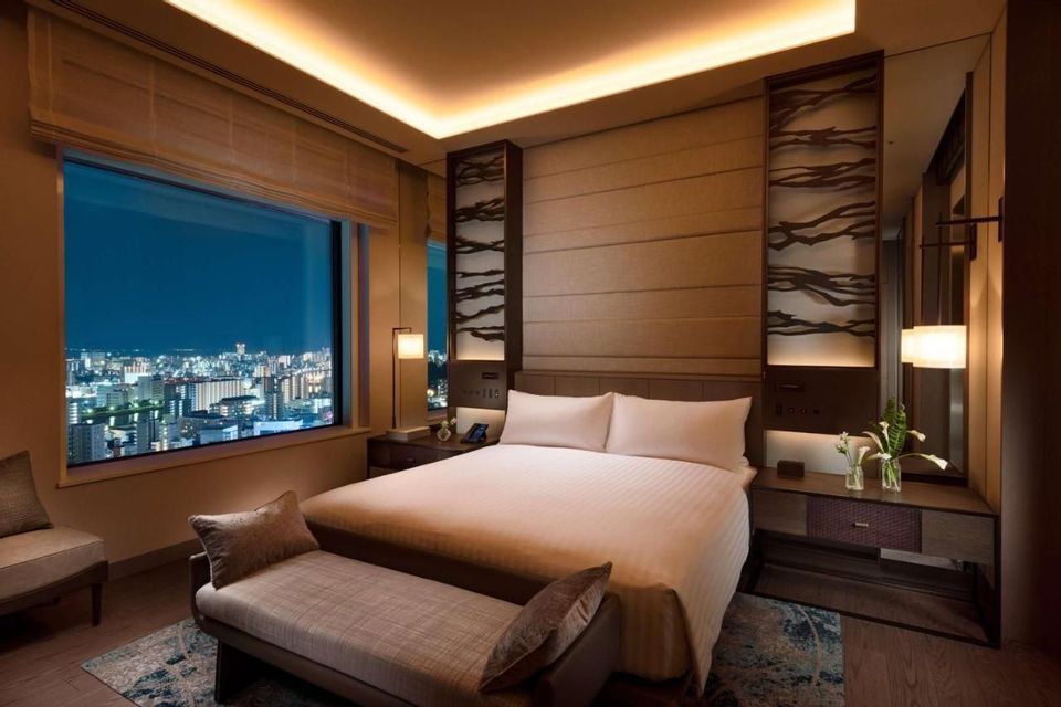 Una moderna camera d'albergo con un grande letto, illuminazione soffusa e una vista notturna sullo skyline della città.