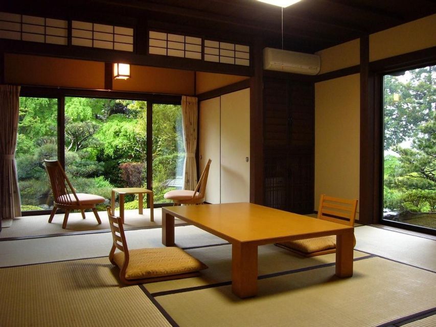 A traditional Japanese room with tatami mats, a low wooden table, and floor chairs overlooks a lush green garden.