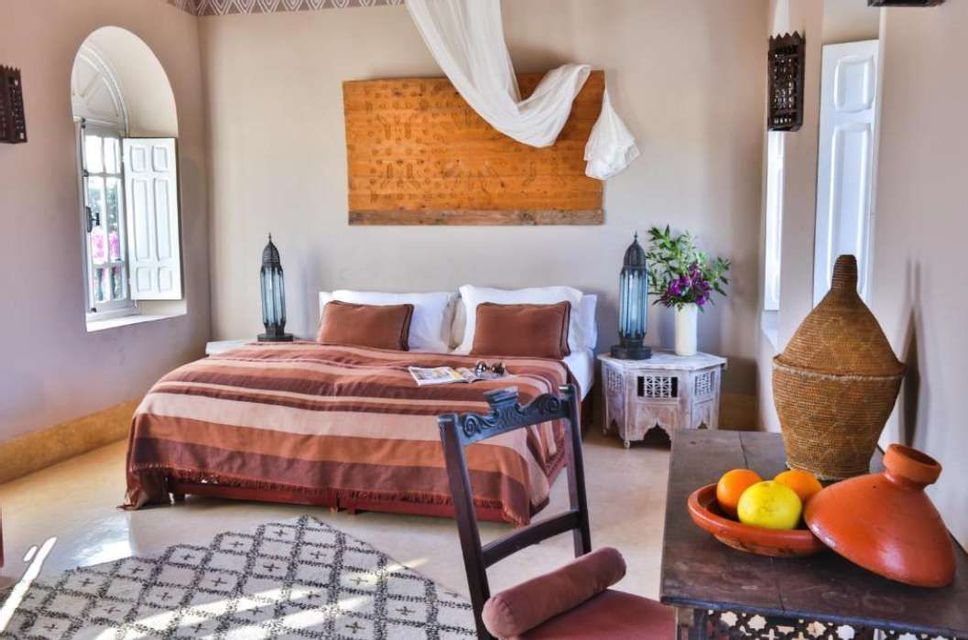 A bedroom decorated in a Moroccan style, featuring a bed with a striped blanket, ornate lamps, and a table with a tagine pot.