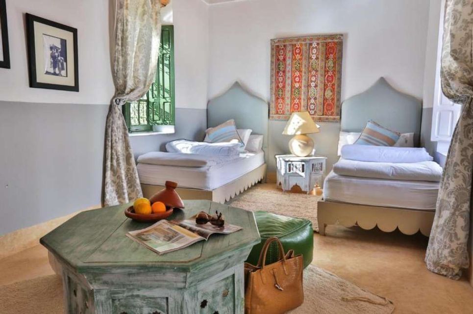 A bedroom with two single beds, a distressed green coffee table, and Moroccan-style decor including a tapestry and a tagine.