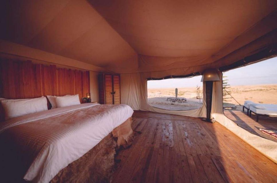 The interior of a luxury tent with a large bed, wooden floors, and an open flap revealing a desert landscape.