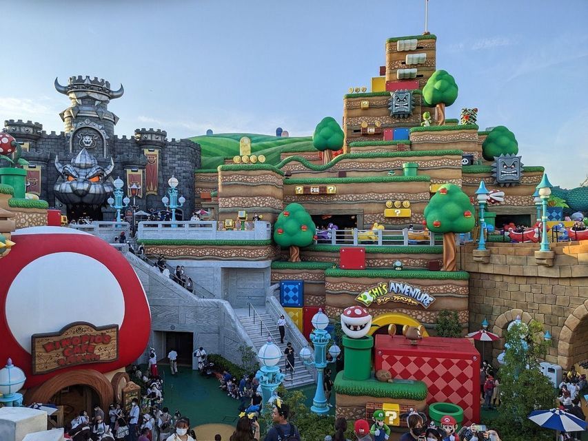 Una vista panoramica del parco a tema Super Nintendo World, che mostra il Castello di Bowser, colline terrazzate e folle di visitatori.