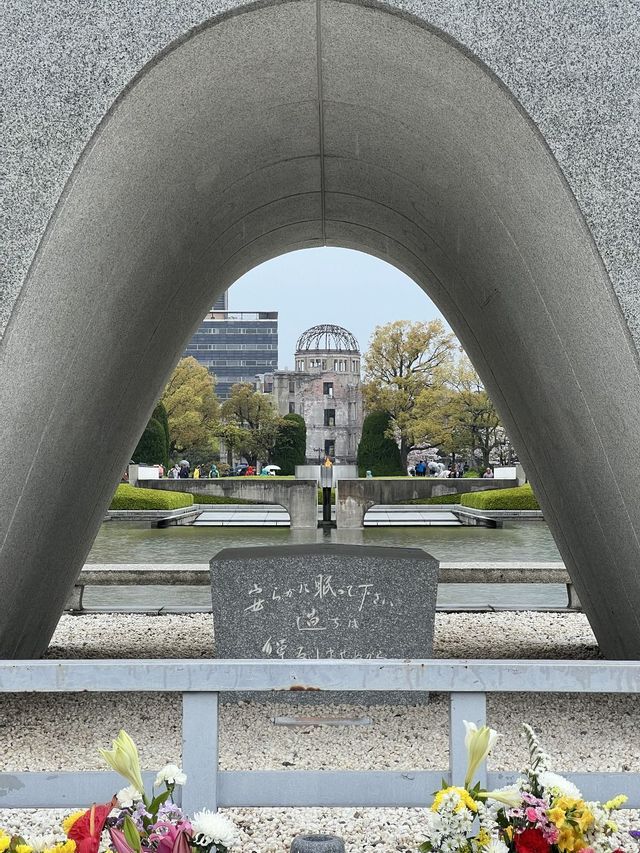 Vista attraverso un grande arco commemorativo in granito che incornicia una rovina a cupola e una fiamma su una vasca d'acqua in un parco.