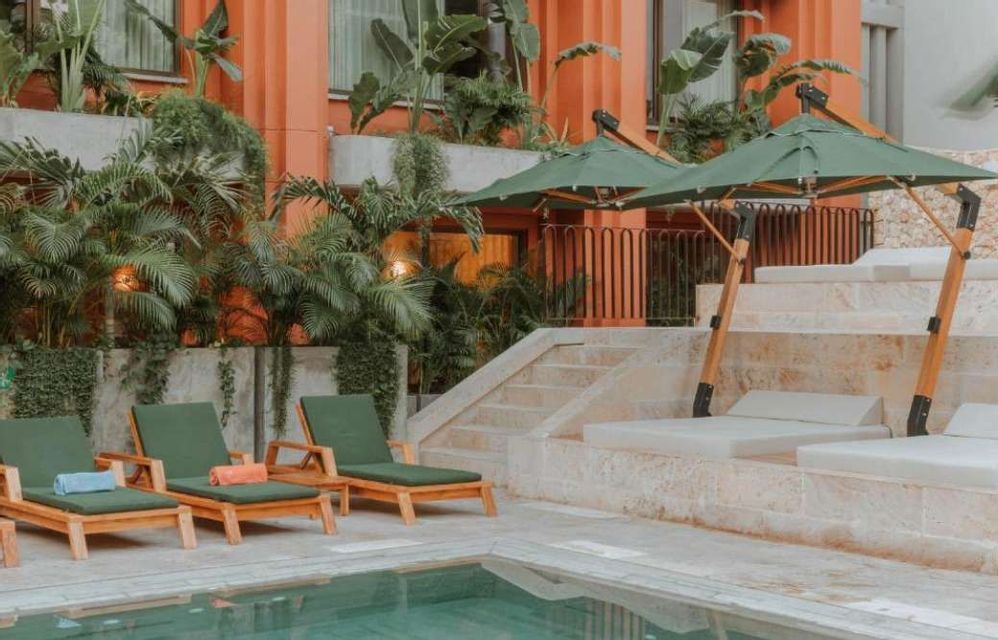 Lounge chairs and umbrellas set up by a swimming pool at a resort with lush plants and a terracotta building.