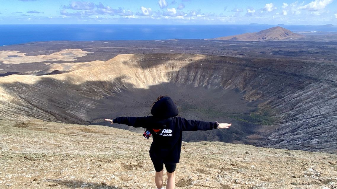 Un accompagnatore WeRoad sta con le braccia aperte sul bordo di un grande cratere vulcanico, affacciato sul mare.