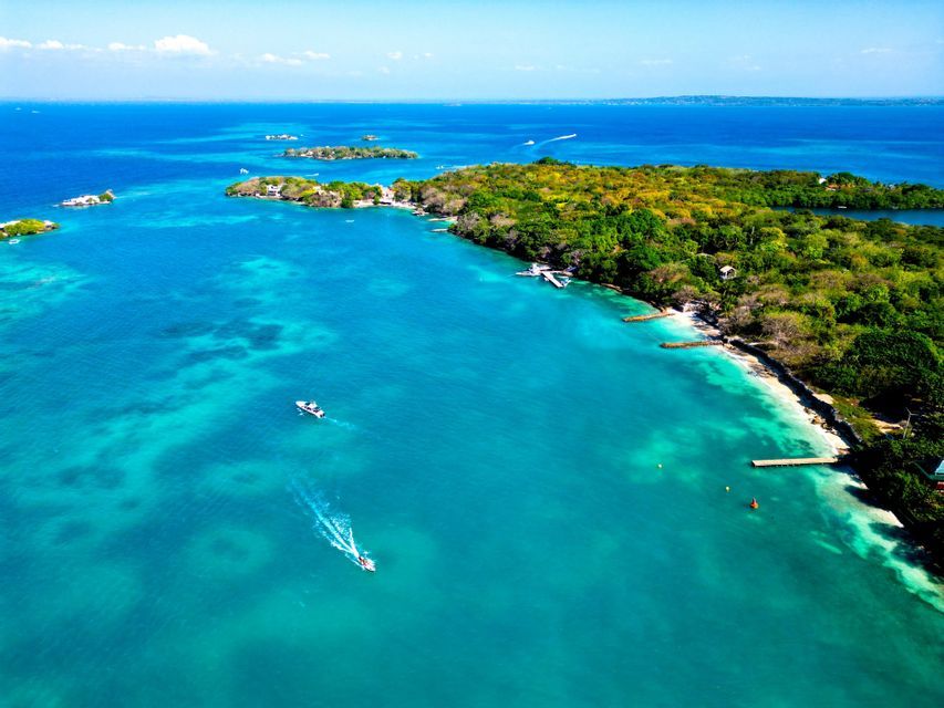 An aerial view of a tropical archipelago with lush green islands, boats sailing on turquoise water, and a clear blue sky.