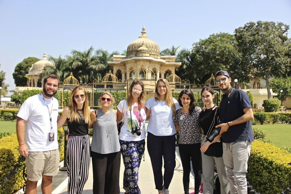 A WeRoad group trip of eight people posing together in a sunny garden in front of an ornate, domed building with palm trees.