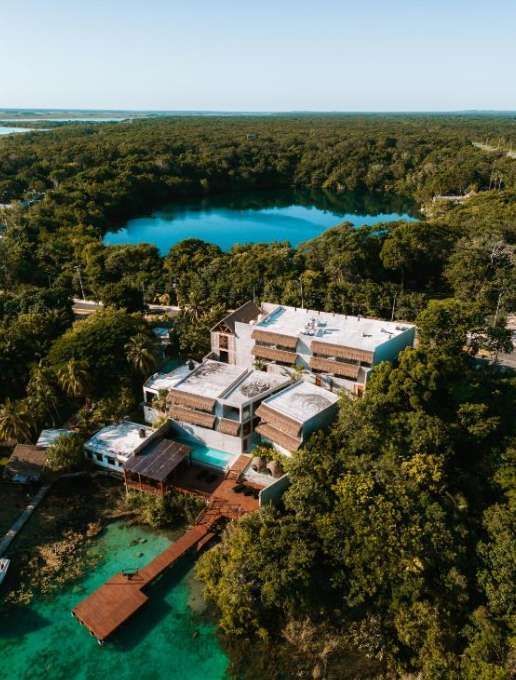 Una vista aerea di un resort moderno con un pontile su una laguna turchese, circondato da una giungla lussureggiante e un lago vicino.