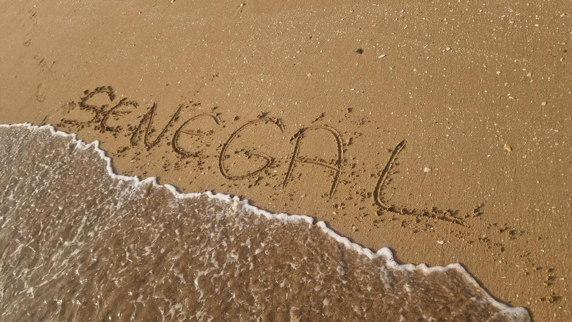 La palabra Senegal escrita en la arena de una playa, mientras una suave ola con espuma blanca baña las letras.