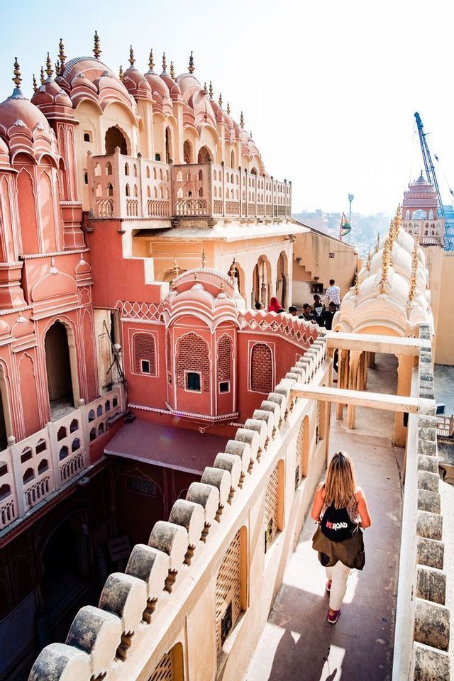 Une femme lors d'un voyage en groupe WeRoad marche sur une haute terrasse, admirant une architecture ornée de couleurs rose et pêche.
