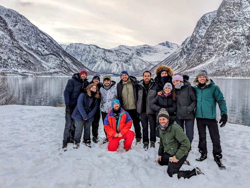 Eine WeRoad-Gruppe lächelt für ein Foto in verschneiter Landschaft mit Fjord und Bergen im Hintergrund.