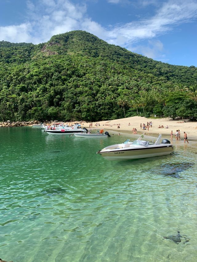 Un viaje en grupo de WeRoad en barco a una cala tropical con agua verde cristalina, una playa de arena y una montaña boscosa.